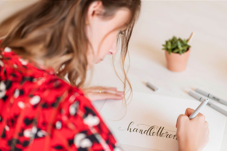 Een persoon schrijft het woord "handlettering" in sierlijk handschrift.