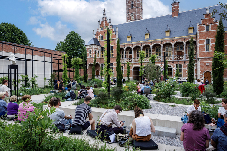 Een tuin waar veel mensen zitten op bankjes en stoelen, gericht naar de gevel van het stadspaleis.