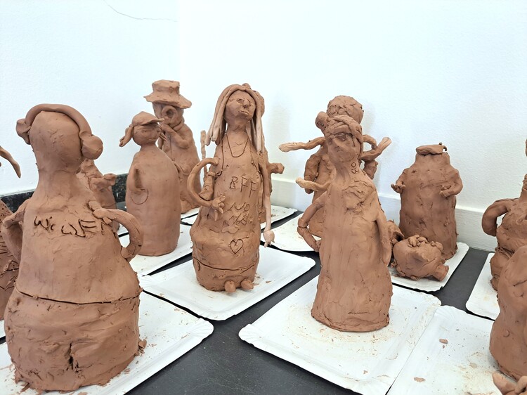 Beeldjes uit bruine klei staan op een witte tafel.