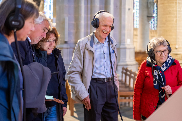 Vijf mensen dragen een hoofdtelefoon en kijken al lachend naar hetzelfde scherm in een kerk.